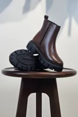 Bota de caña corta color marrón, con cierre lateral y suela track negra de goma con plataforma.