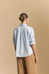 Camisa de corte clásico y holgado, confeccionada en tela blanca, con cuello camisero, cierre frontal de botones de nácar y mangas largas con puños abotonados.