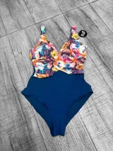 Malla entera plus size con diseño combinado, parte inferior negra y parte superior con estampado floral en tonos amarillos, rojos y celestes, con escote en V cruzado.
