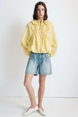 Chaqueta de nylon color amarillo pastel, con cuello subido y capucha. Presenta cierre frontal con cremallera, mangas largas con puños elásticos y detalle de lazadas ajustables en el frente. El bajo cuenta con cordón elástico y stoppers para un ajuste personalizado.