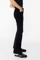 Pantalón de jean tipo pana color negro, de corte acampanado y tiro medio, con cierre frontal y bolsillos laterales.