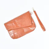 Sobre de mano color marrón con textura símil piel de cocodrilo y correa de muñeca desmontable.
