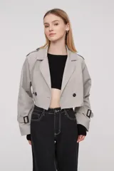 Trinchera corta color gris claro, con solapas, doble botonadura, cinturón y mangas largas con trabillas ajustables.