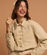 Campera color beige confeccionada en sarga de algodón, de corte regular, con cuello camisero, cierre abotonado, manga larga, bolsillos frontales y recortes.