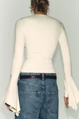 Camiseta de cuello redondo y manga larga, confeccionada en tejido rib con mezcla de lyocell. Presenta un diseño ajustado con terminación de volantes en los puños y bajo recto.