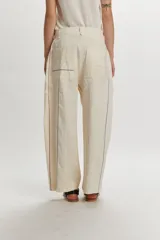 Pantalón de corte relajado, color beige, con diseño de rayas sutiles verticales y líneas de colores en contraste. Presenta cierre frontal con botón y trabillas para cinturón.