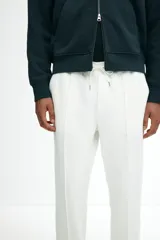 Pantalón tipo jogger de punto en color blanco, con pliegue cosido frontal, cintura elástica con cordón ajustable, bolsillos laterales y un bolsillo insertado trasero. Corte regular.