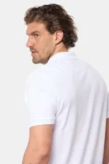 Remera polo de piqué color blanco, con cuello y puños en rib, cierre frontal con botones y logo bordado pequeño en el pecho.
