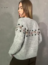 Saco cardigan gris de punto con detalles en tonos chocolate y diseño estampado en la parte superior y mangas. Cuenta con cierre frontal de botones y ribetes marrones en los bordes.