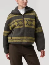 Sweater polar de cuello alto y cierre medio con detalles en cuero sintético, de color verde oscuro con estampado de patrones tradicionales en tono verde claro. Cuenta con mangas largas y diseño holgado.