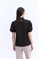 Camisa negra de manga corta abullonada, con cuello clásico y cierre frontal de botones.
