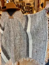Poncho de lana virgen tejido en telar con diseño geométrico a rayas en tonos gris, marrón y celeste, con apliques de cuero en el escote y flecos en el ruedo.
