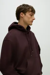 Sudadera con capucha color borgoña, de corte holgado, con cordones ajustables en la capucha y bolsillo canguro frontal.