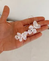Aros colgantes con diseño de flores blancas de resina y centro de perla, montados sobre gancho de metal dorado.