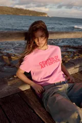 Remera de algodón color rosado con efecto lavado, de corte regular y cuello redondo, con texto rojo estampado en el frente que dice 'CENTER OF ATTENTION'.