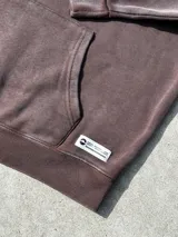 Buzo canguro marrón con capucha y cordones, de corte amplio y estilo urbano.