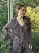 Camisa de lino azul marino con volados en cascada a lo largo del frente y en los puños de las mangas largas. Presenta un escote en V con un botón de nácar visible.