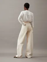 Blusa de manga larga color blanco roto, confeccionada en tejido Georgette de poliéster reciclado. Presenta un escote sin cuello con abertura en V y detalles plisados en los hombros y la espalda.