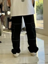 Pantalón cargo de jean negro con múltiples bolsillos utilitarios y costuras visibles en contraste de color blanco.