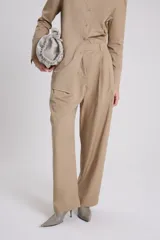 Pantalón sastre de corte recto en tejido plano de algodón color beige, con detalle de solapa asimétrica en la parte superior izquierda.