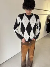 Sweater de punto con diseño de rombos en blanco y negro, con detalles de líneas finas en color marrón. Presenta cuello redondo y mangas largas con puños acanalados.