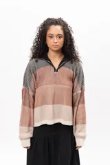 Buzo de tejido de punto con diseño a rayas horizontales en tonos tierra, negro y crema. Presenta cuello alto con cierre frontal parcial, mangas largas con puños ajustados y corte holgado.