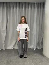 Remera blanca de algodón con estampado gráfico estilo oriental en colores rosa y negro. Presenta un diseño asimétrico con caracteres en la parte superior derecha y lateral inferior izquierdo.