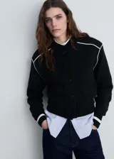 Chaqueta estilo bomber de tejido de punto en color negro, con cuello redondo, cierre frontal de botones y detalles de rayas blancas en contraste en los hombros y puños.