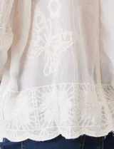 Camisa de algodón color gris con bordados florales en el frente y las mangas. Tiene cuello con solapa y cierre frontal con botones.