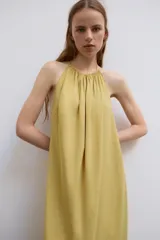 Vestido midi color amarillo con cuello halter, espalda descubierta y lazada en el mismo tejido.