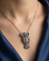 Dije con forma de búho elaborado en plata 925 con detalles en lámina de oro 18k en los ojos. Presenta un diseño detallado con texturas grabadas en las alas y el cuerpo.