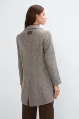 Saco corto entallado de lana fina, con cuello solapa, manga larga y cierre frontal con botones. Presenta un diseño clásico con textura de espiga en tonos tierra.