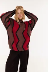 Sweater de punto con diseño geométrico en zigzag, combinando franjas en color marrón, rojo y negro. Presenta cuello redondo, mangas largas y un corte holgado.