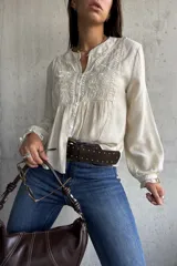 Camisa beige de manga larga con cuello mao y escote en V. Presenta detalles bordados en el canesú y los hombros, y volados en los puños.