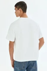 Remera de punto de algodón de peso medio, color blanco, con cuello redondo ribeteado, hombros caídos, bajo recto y corte relajado.