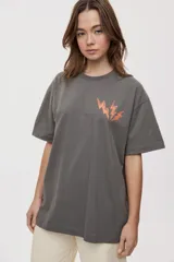Remera de manga corta con calce oversized y cuello redondo, color gris oscuro, con pequeño gráfico de rayos naranjas en el frente.
