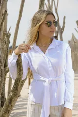 Camisa blanca de manga larga con cuello clásico, ajuste en la cintura mediante lazo del mismo tejido y hombros ligeramente abullonados.