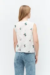 Chaleco blanco de broderie con bordados florales, escote en V y cierre con lazos.