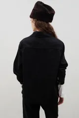 Camisa de denim negro con estampa floral blanca, cuello camisero, cierre frontal con botones y mangas largas.