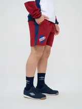 Bermuda deportiva Umbro del Club Nacional de Football, color azul marino, con cordón ajustable en la cintura, bolsillos laterales, el escudo del club en una pierna y el logo de la marca en la otra.