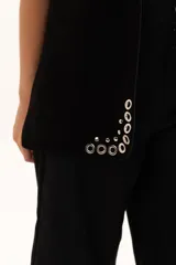 Chaleco negro de gamuza con diseño sin mangas, decorado con ojales metálicos plateados a lo largo de los bordes frontales y sisas.