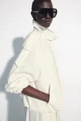Chaqueta oversize negra confeccionada en hilatura con mezcla de modal, de corte fluido. Cuenta con cuello subido, manga larga con puños elásticos, bolsillos de vivo en el delantero y trabillas en los hombros. El bajo es abullonado con elástico y el cierre frontal es con botones a presión.