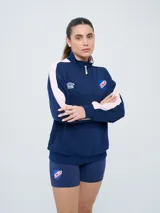 Buzo de felpa azul marino con medio cierre, cuello alto, bandas laterales en tono rosado y bolsillo frontal tipo canguro. Presenta el logo de Umbro y el escudo del Club Nacional de Football bordados.
