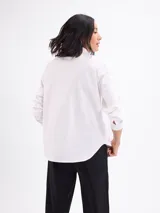 Camisa blanca de manga larga, con cuello clásico y cierre frontal de botones.