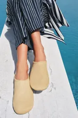 Zapato tipo mule de mujer confeccionado en piel con textura de pelo en color beige. Presenta un diseño de punta redonda y suela plana en contraste.