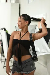 Top negro estilo bandeau con escote fruncido y detalle de lazo central. Presenta una capa inferior de tela transparente que cae en forma de lazo largo. Se sujeta al cuello con una tira fina.