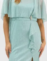 Vestido midi de tejido metalizado color turquesa, con sobrecapa de tul liviano sobre los hombros, detalle de pedrería en la cintura, volado lateral y tajo frontal.