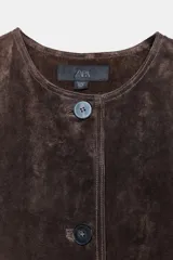 Abrigo marrón de gamuza con cuello redondo, manga larga, bolsillos delanteros y cierre frontal con botones.