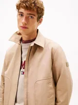 Campera Tommy Hilfiger modelo Ivy, color beige, confeccionada en tejido técnico impermeable y resistente al viento. Cuenta con cuello clásico, cierre frontal de cremallera, bolsillos laterales ribeteados y parche engomado en la manga.