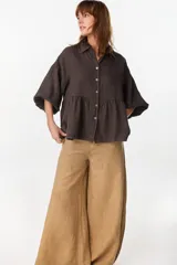 Camisa de lino marrón oscuro con silueta holgada, cuello camisero, cierre frontal de botones claros, mangas voluminosas y detalle de frunces en la cintura.